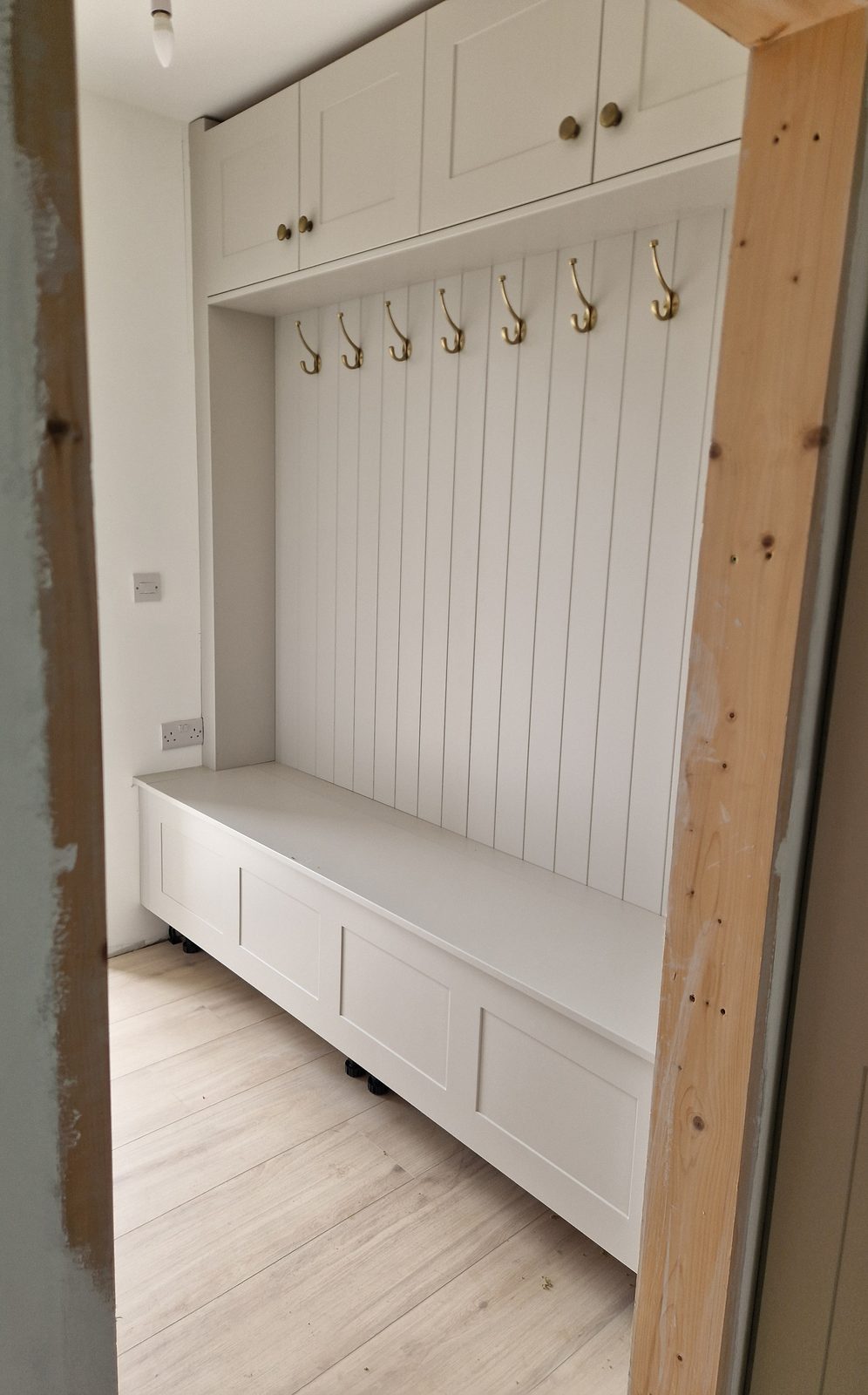 White boot room bench with brass coat hooks and tongue-and-groove